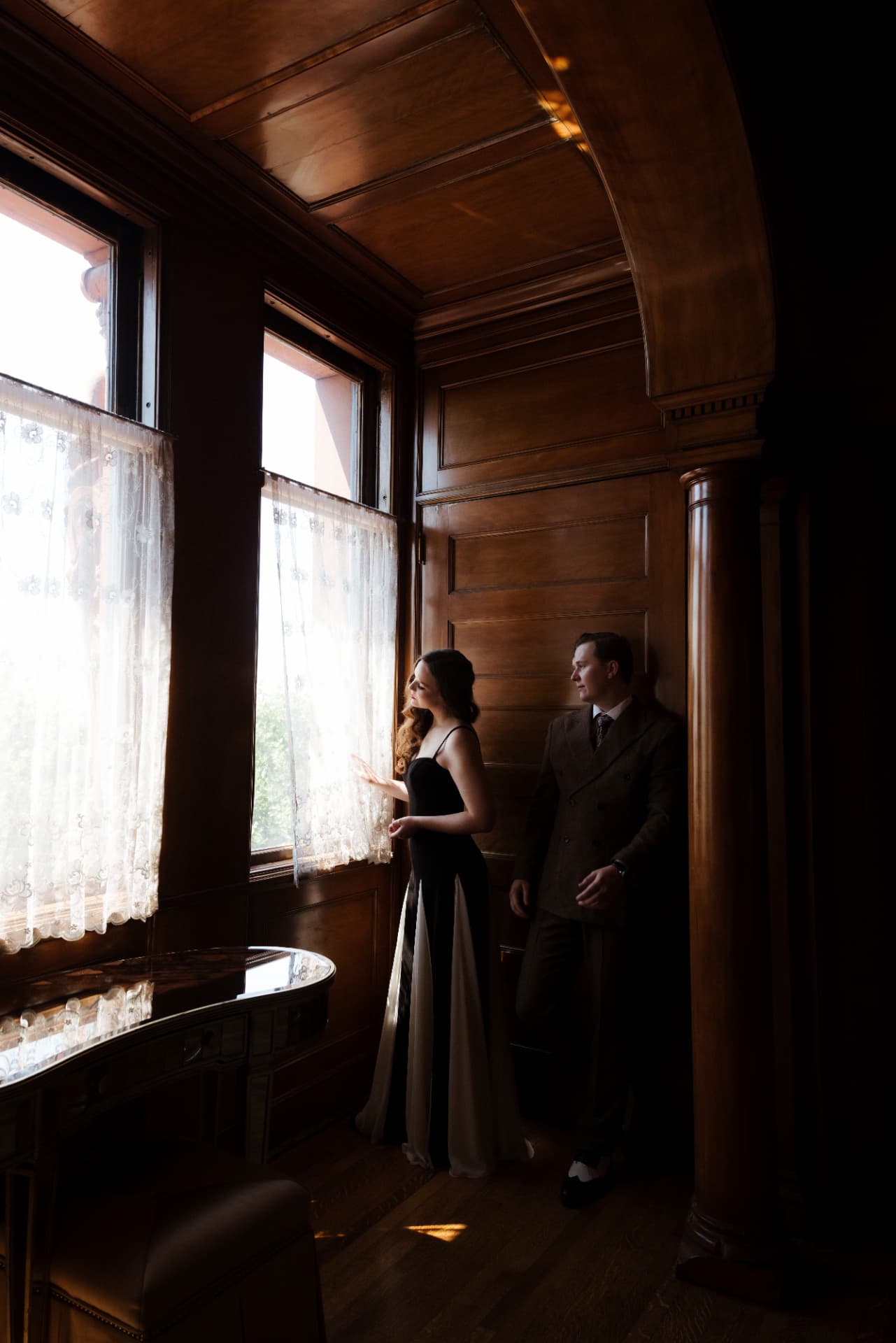 Drew and Olympia by a lace-curtained window in warm afternoon light