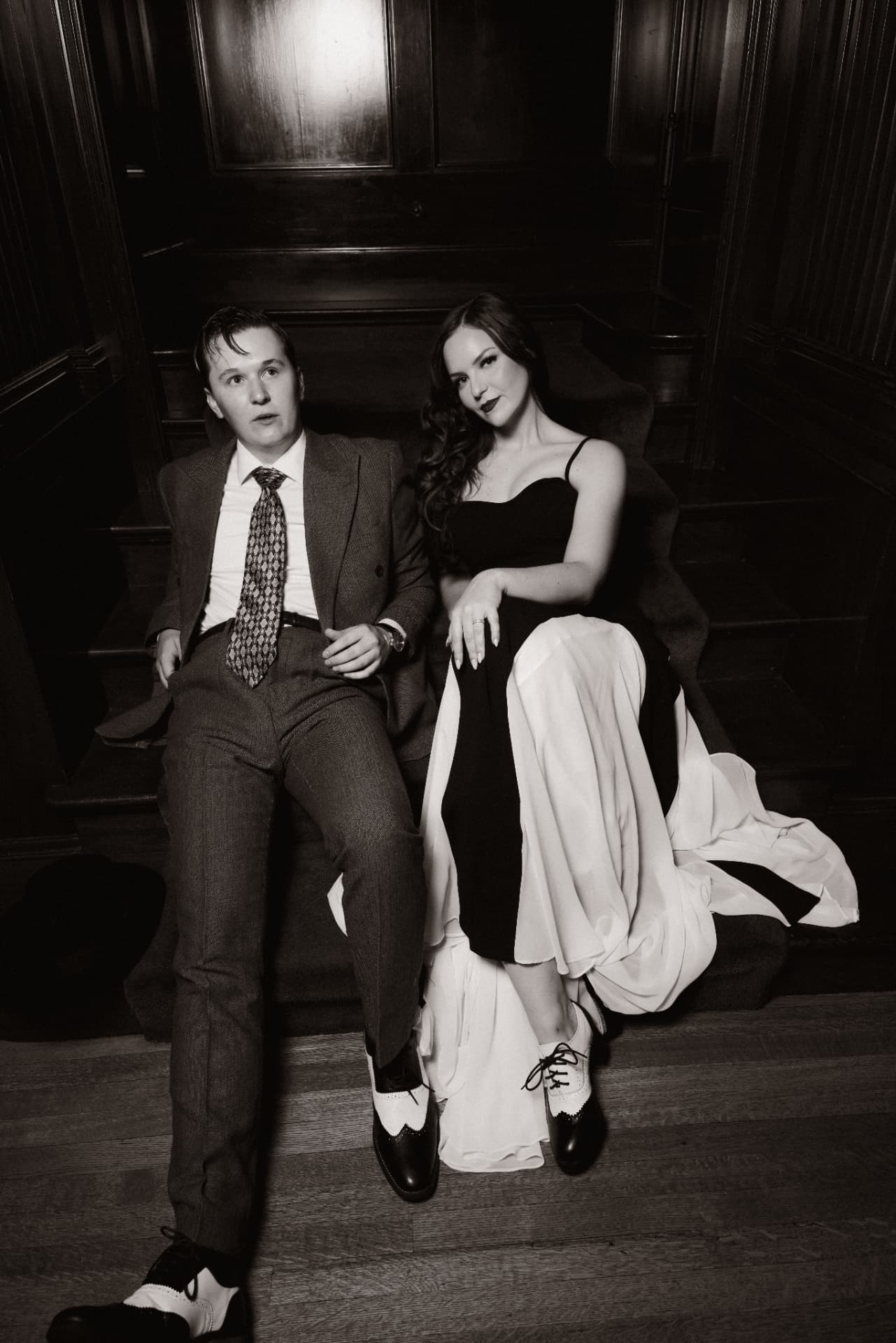 Drew and Olympia lounging on a dark wood staircase