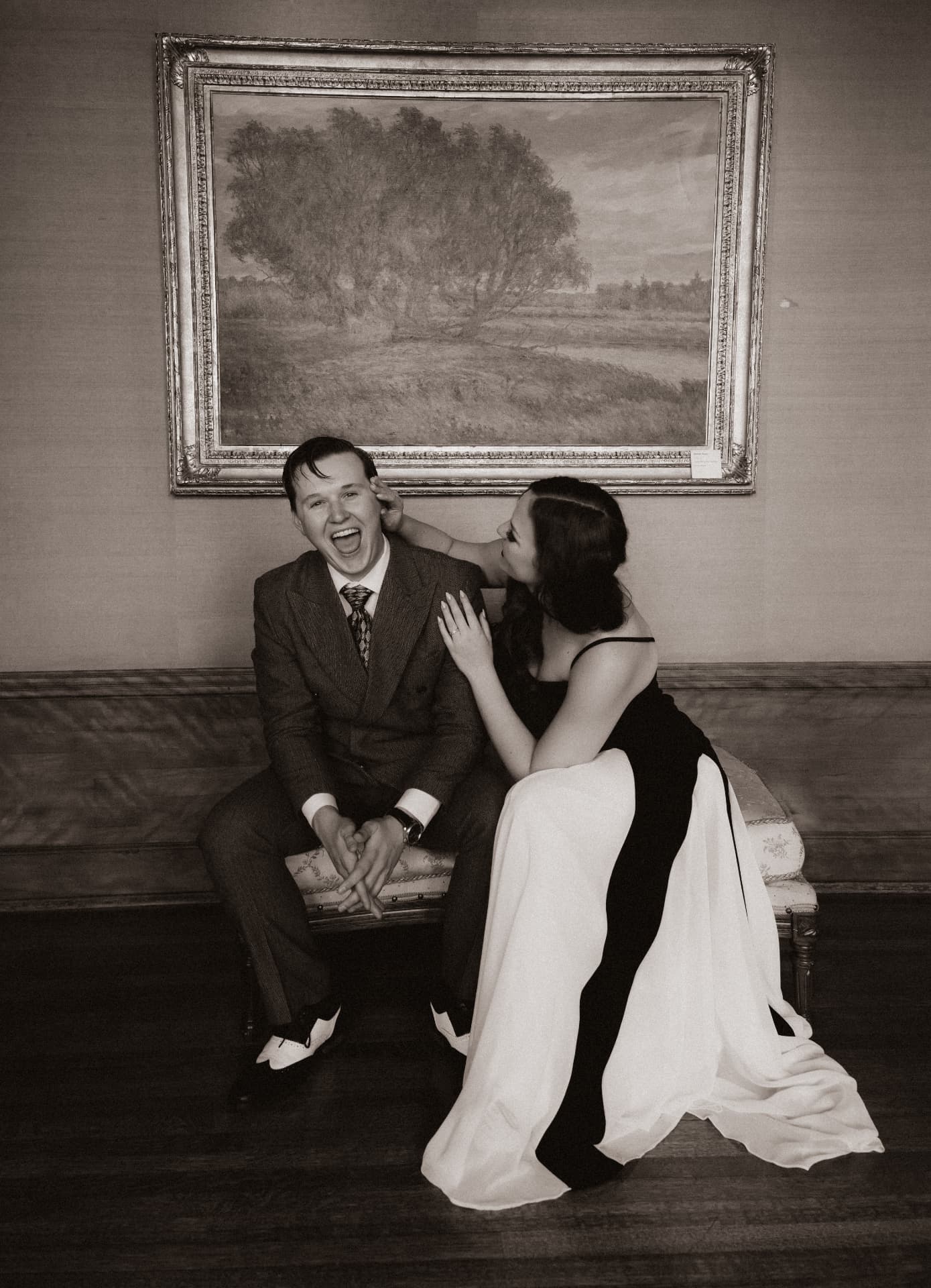 Drew and Olympia laughing together beneath a framed landscape painting